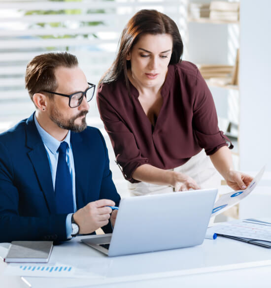 Two colleagues reviewing documents and a laptop at a desk